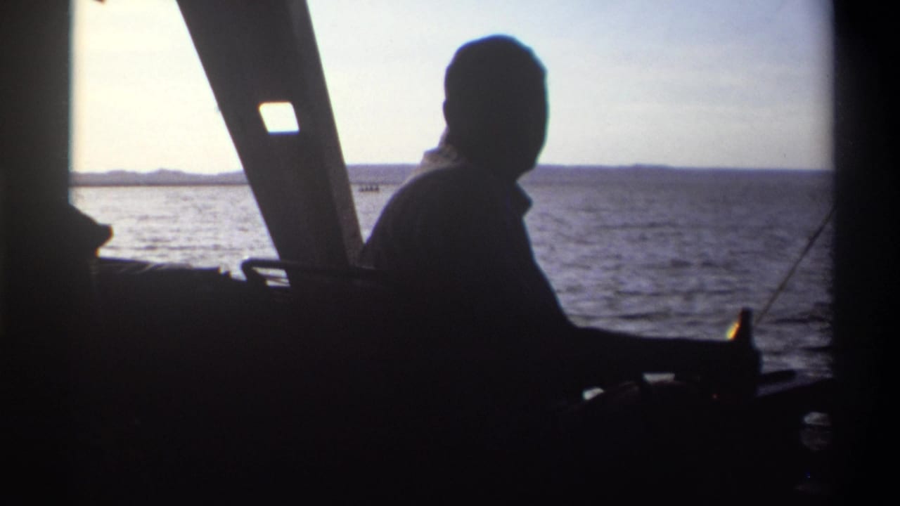 The silhouetted man remains inside the boat as the 8mm camera records water, sky, and a low shoreline in Nigeria, 1969.