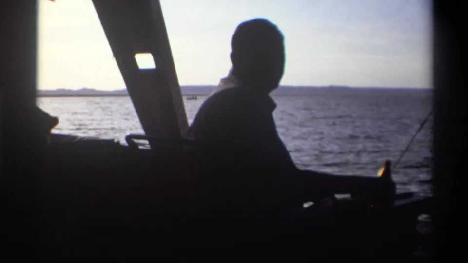 The silhouetted man remains inside the boat as the 8mm camera records water, sky, and a low shoreline in Nigeria, 1969.