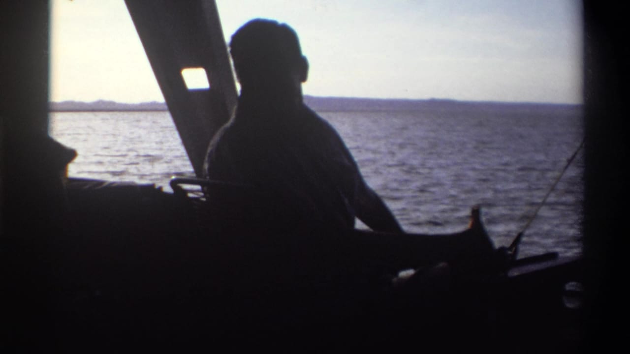 A man in silhouette turns inside the boat, with Nigeria's open water and distant shoreline visible through the bright window in 1969 footage.
