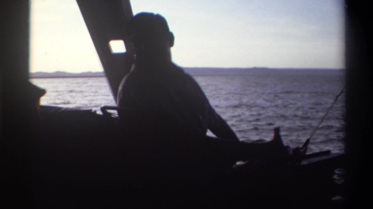1969 Nigeria home-movie frame showing a silhouetted man seated aboard a boat against bright sea and distant land.