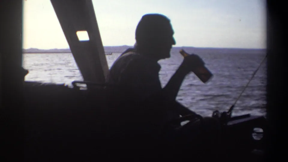 1969 Nigeria frame showing a man in profile silhouette raising a bottle while seated aboard a boat on open water.