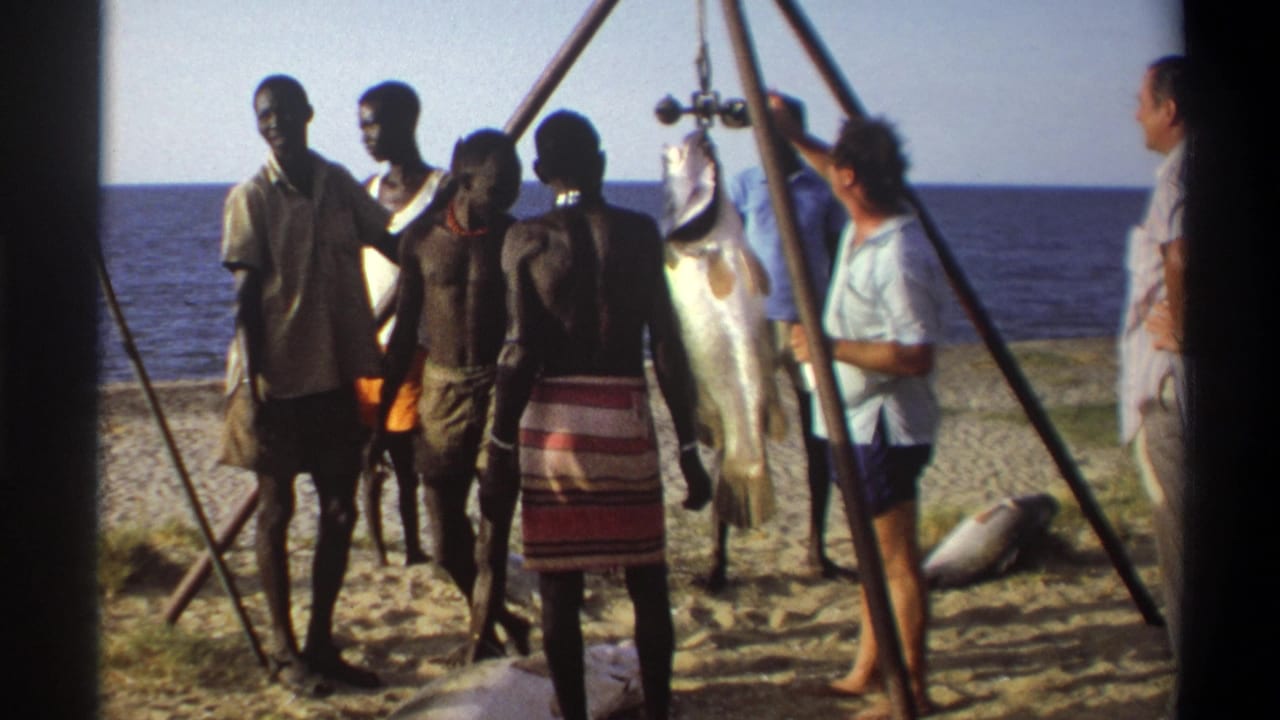 Men in a beachside market scene in Nigeria stand around a large fish suspended from a bamboo weighing frame.