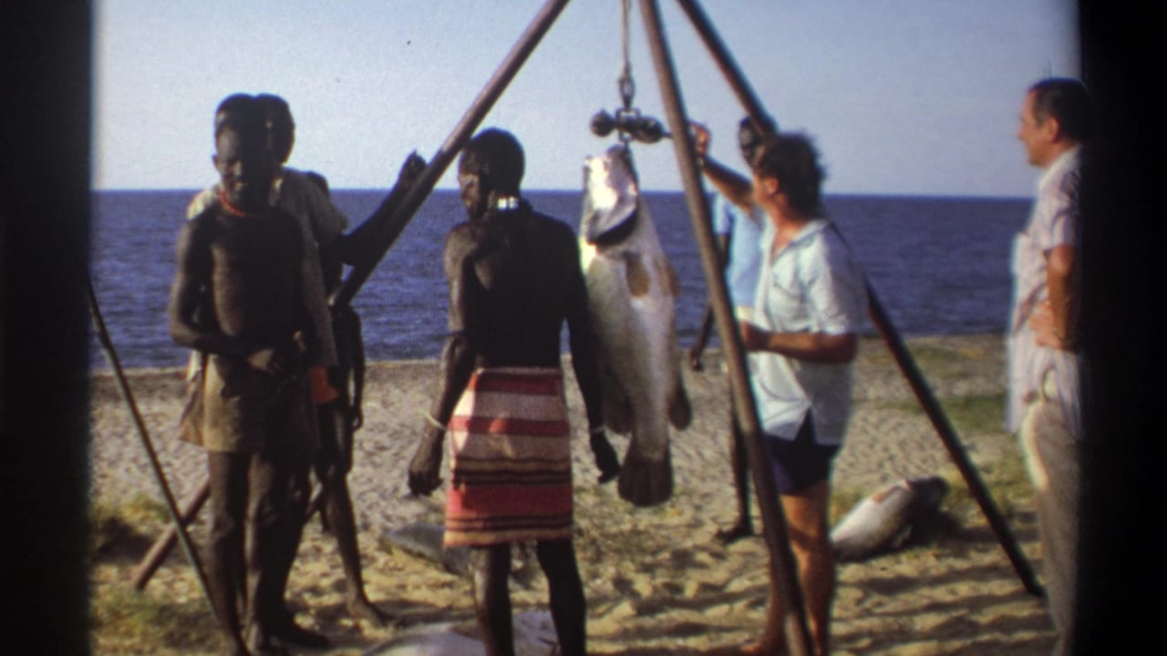 1969 Nigeria beach scene with a suspended fish, local men nearby, and visitors observing beside the shoreline.