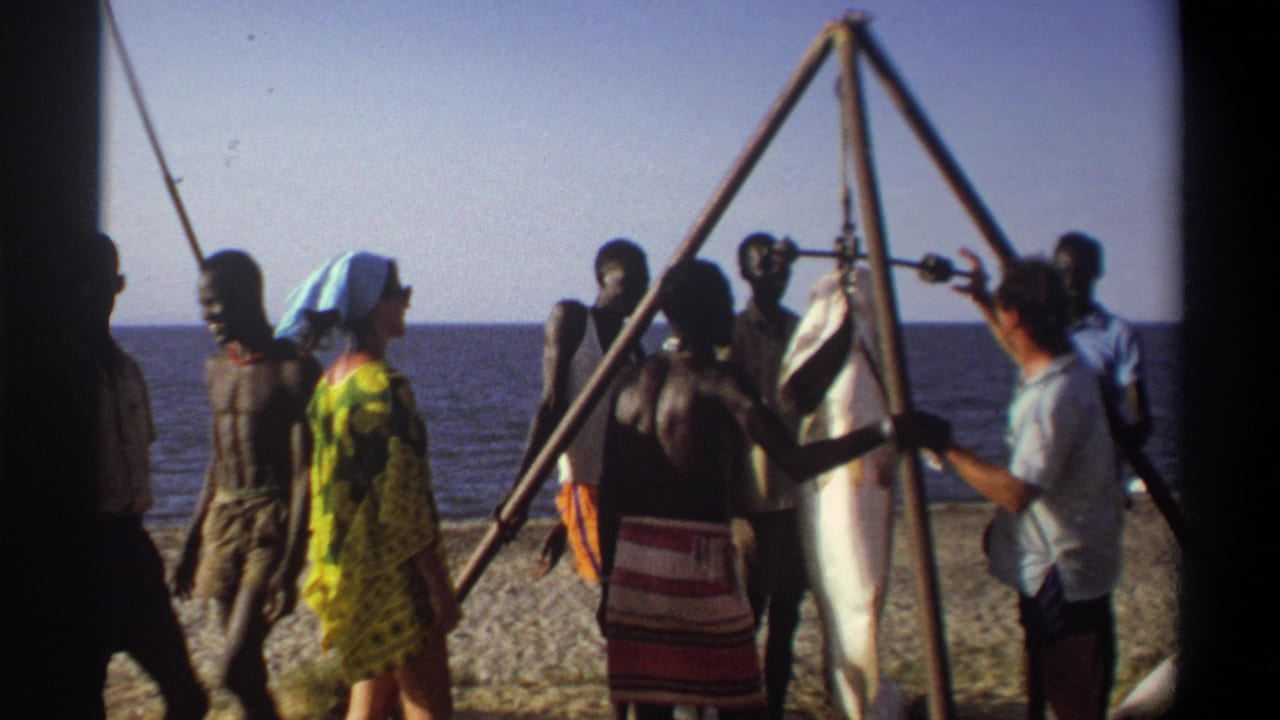 Nigeria 1969 8mm frame with adults beside a suspended large fish, the sea behind them and strong sun across the beach.