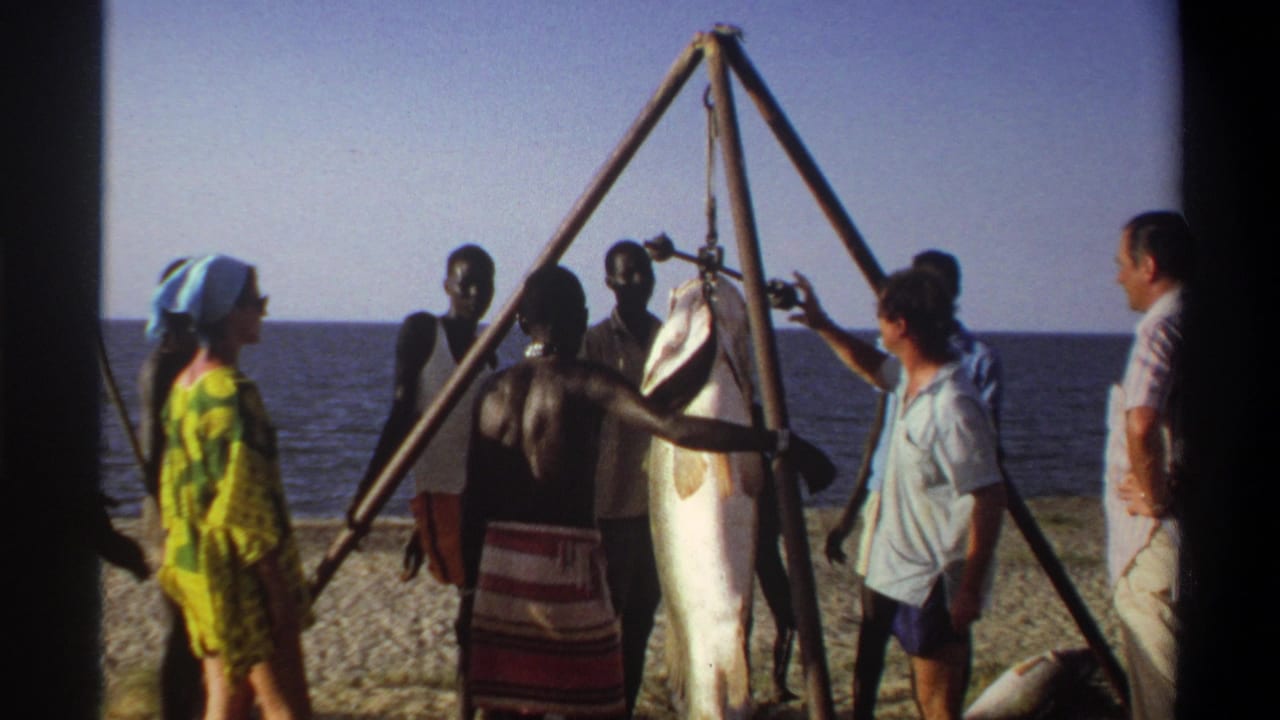 Late-1960s Nigerian beach footage shows people surrounding a large fish hanging from a triangular wooden frame near the sea.