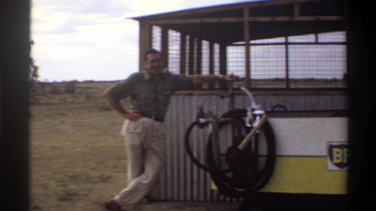 In Nigeria in 1969, a man stands beside a corrugated BP fuel station with pump hoses and open grassland behind him.