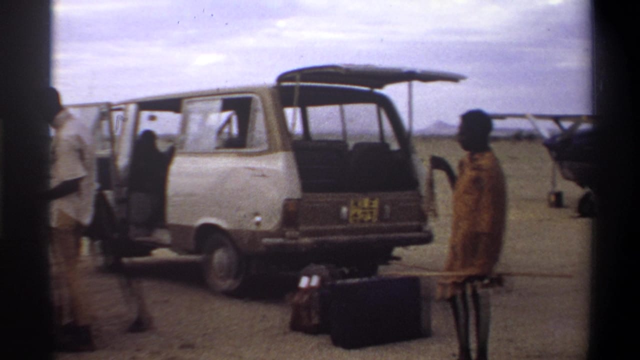 1969 Nigeria home-movie frame showing people loading or unloading near an open van, with luggage in the foreground.