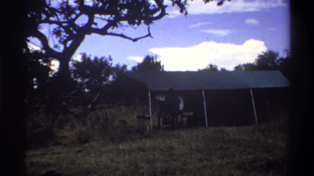 1969 Lagos frame with a dark tent-like structure, tree branches overhead, and a small person partly silhouetted near the opening.