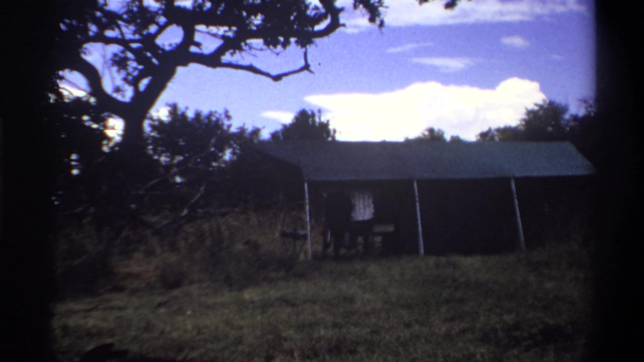 1969 Lagos frame showing a tent-like shelter under a tree canopy, with a small person partly visible near one side.