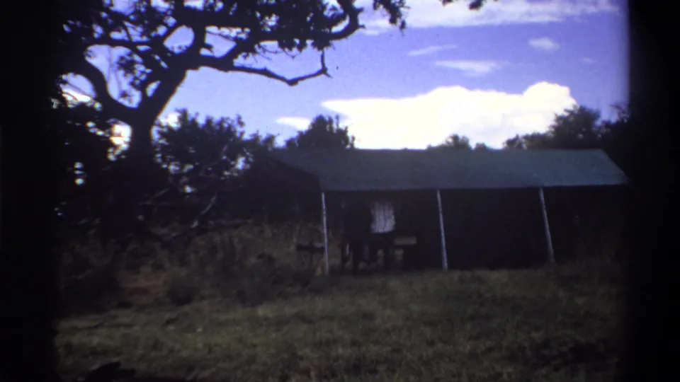 1969 Lagos frame showing a tent-like shelter under a tree canopy, with a small person partly visible near one side.