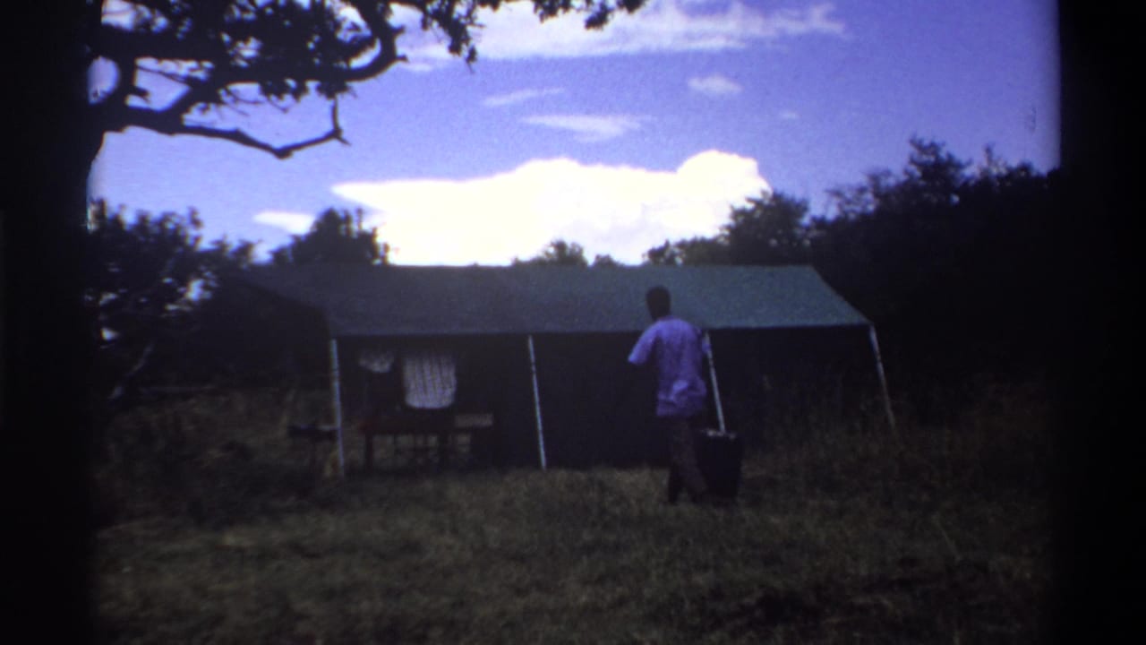 1969 Lagos frame showing a man with luggage approaching a canvas tent, with another person faintly visible in the shaded interior.