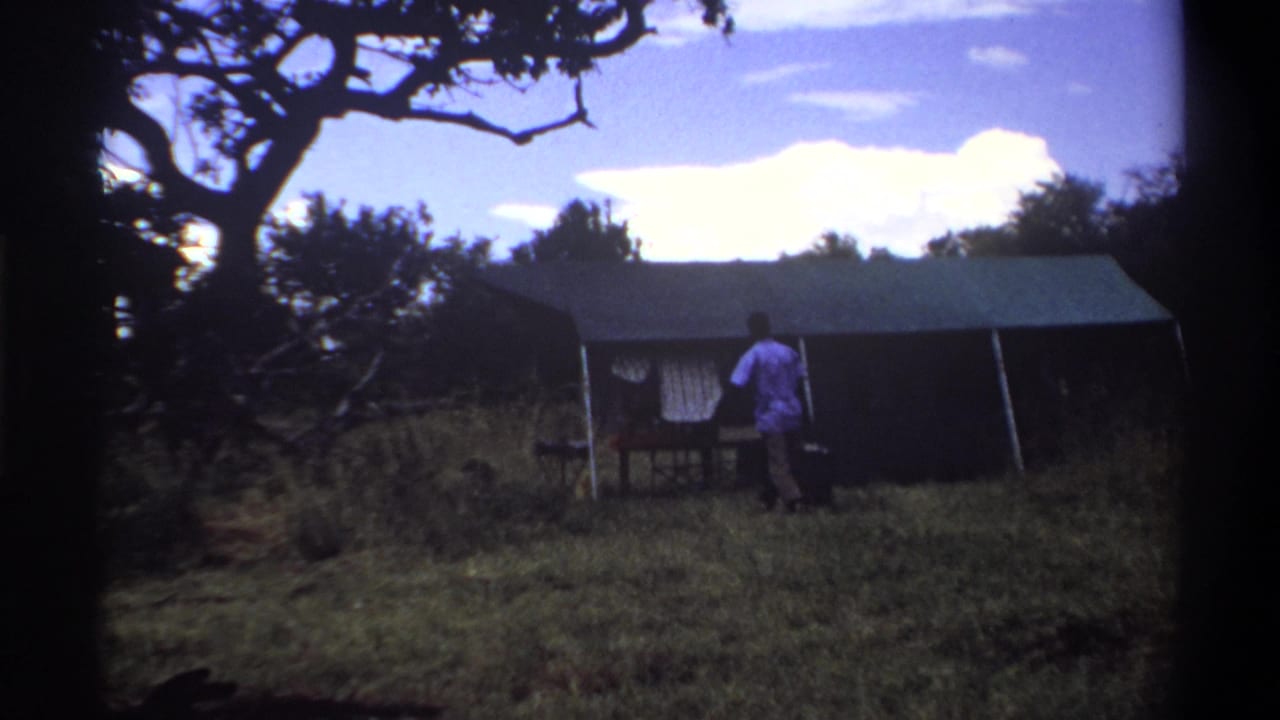 In Lagos, Nigeria, 1969, a man in a light shirt carries an object toward a canvas tent in a grassy clearing.