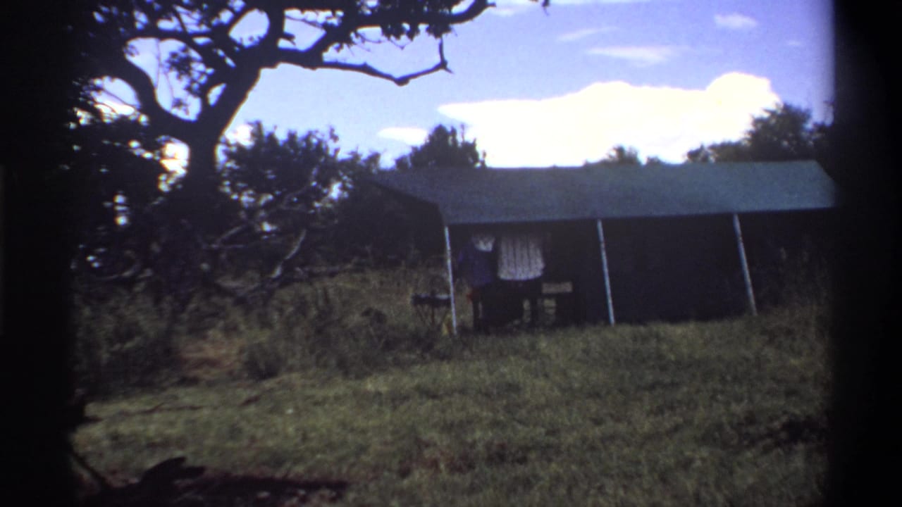 The final 1969 Lagos frame holds on the canvas tent, table, grass, and shaded tree framing as the man is partly hidden near the entrance.