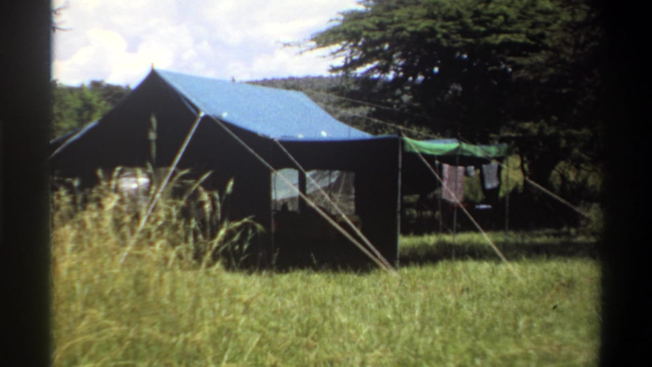 1969 Lagos home-movie frame showing a canvas tent in a grassy clearing with trees, guy ropes, and clothes hanging nearby.