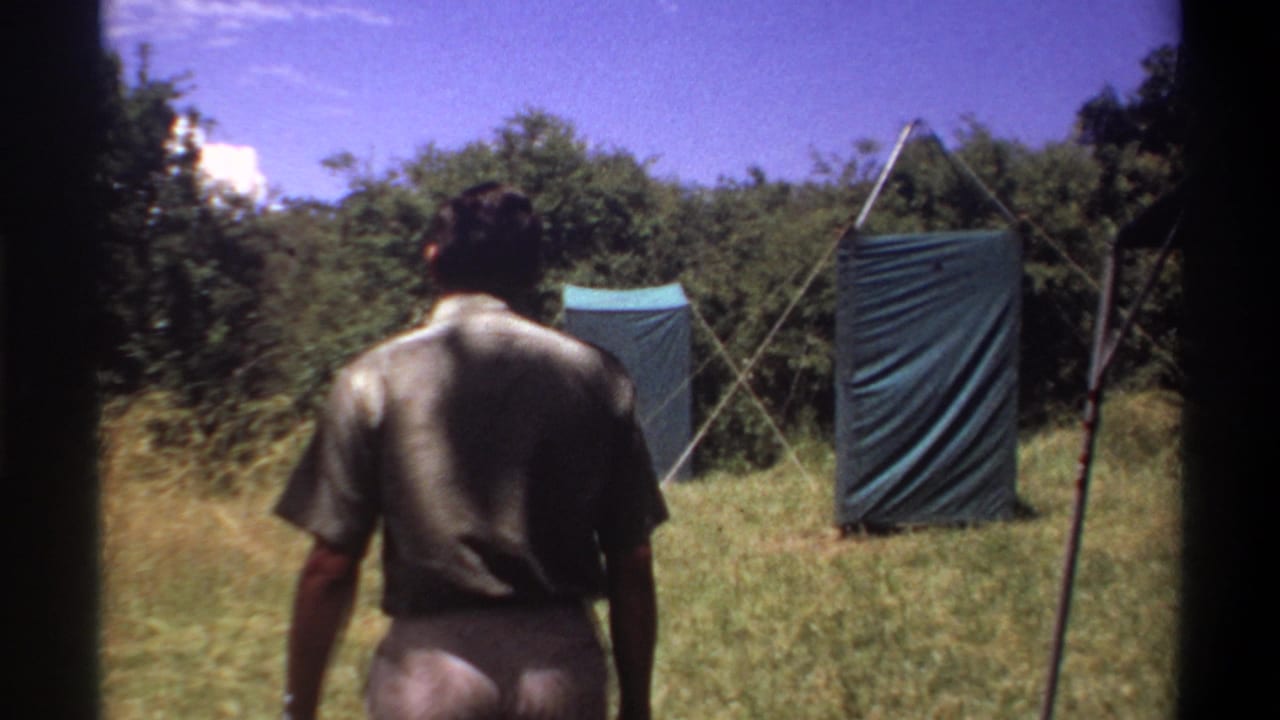 Man seen from behind walking across grass toward two blue-green tarp shelters.