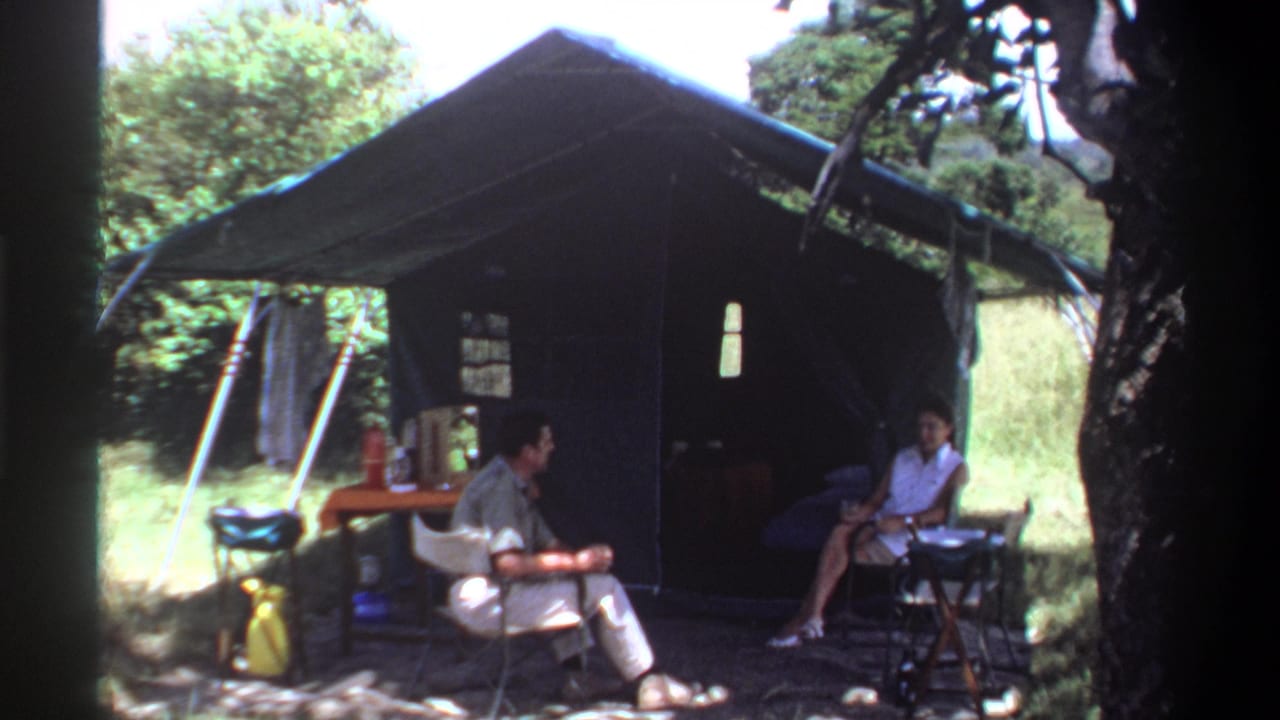 1969 Lagos home-movie frame showing two adults relaxing outside a green canvas tent in a wooded campsite setting.