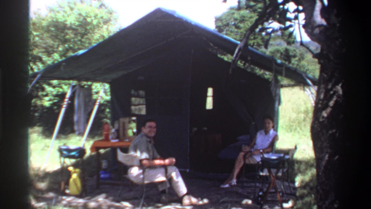 A man and woman sit outside a tent, with the man turned toward the camera.