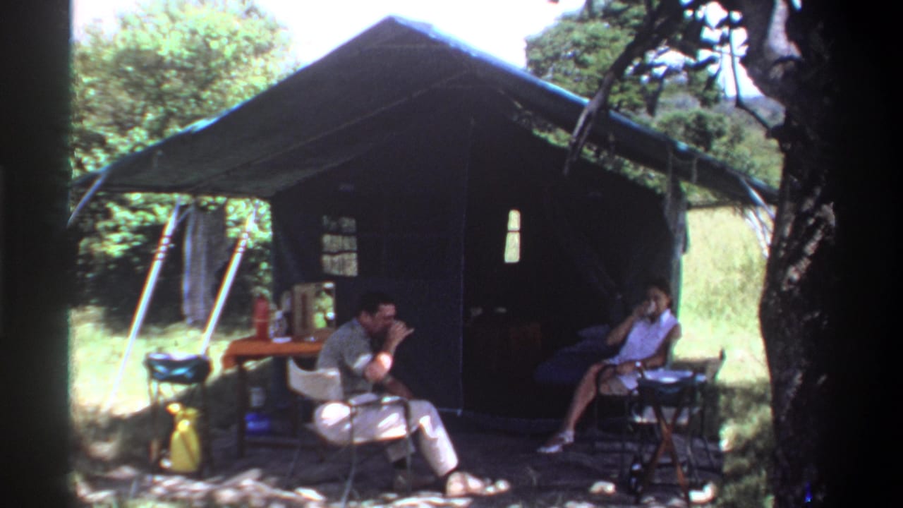 In Lagos, Nigeria, 1969, two adults sit outside a dark tent with folding chairs, a small table, and greenery around them.