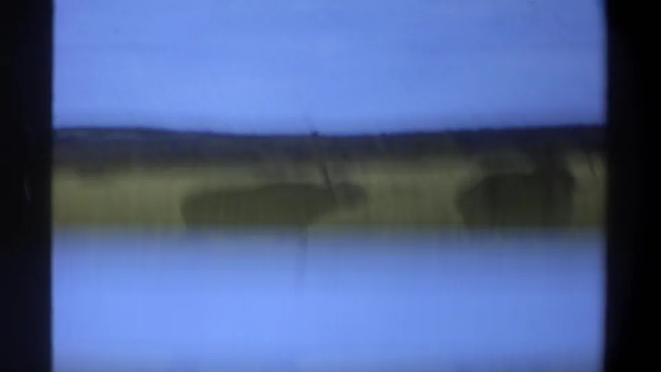 Transition frame from the 1969 Lagos, Nigeria 8mm scan, with blue sky, distant horizon, and blurred grass visible through film-gate edges.