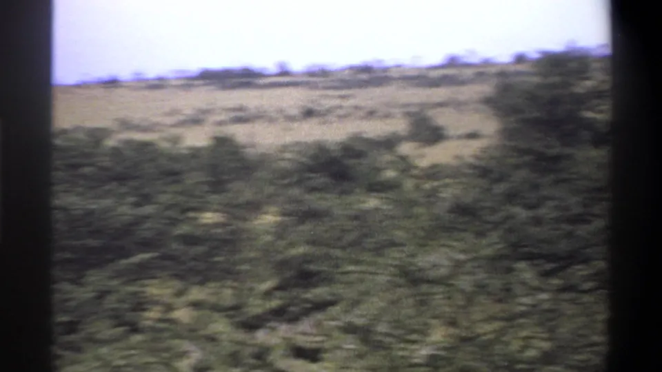 1969 Nigeria 8mm frame showing empty scrubland, low bushes, dry grassland, pale sky, and dark film borders.
