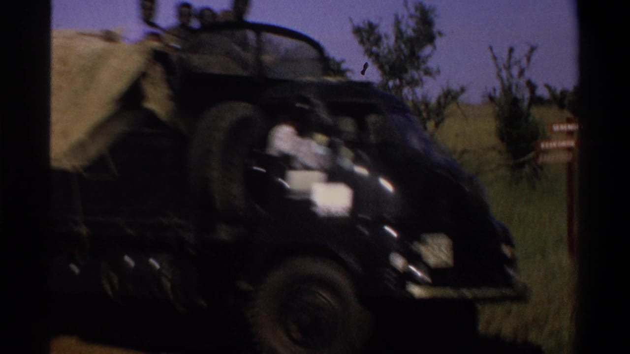 1969 Lagos, Nigeria roadside frame showing a black truck with visible riders passing vegetation and a small sign.