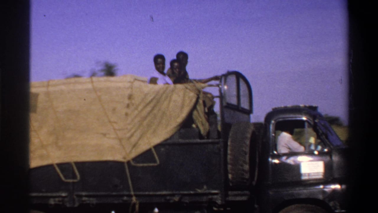 Covered utility truck with men riding on top and a driver visible in the cab.