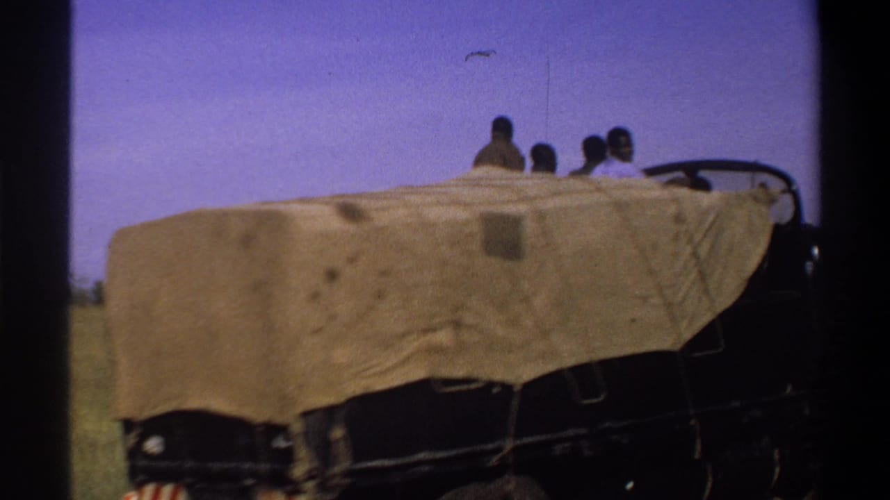 Side view of a tarp-covered truck with several passengers visible above it.
