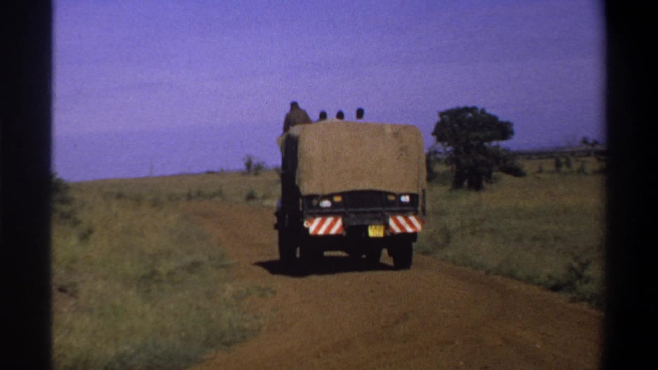 1969 Lagos, Nigeria 8mm frame showing a canvas-covered truck receding on an unpaved road with people riding on top.