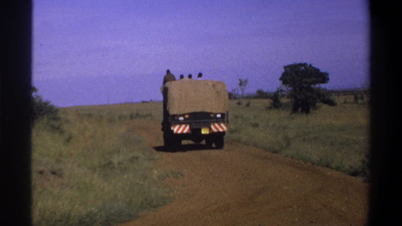 Covered truck farther down a dirt roadway with grass and trees nearby.