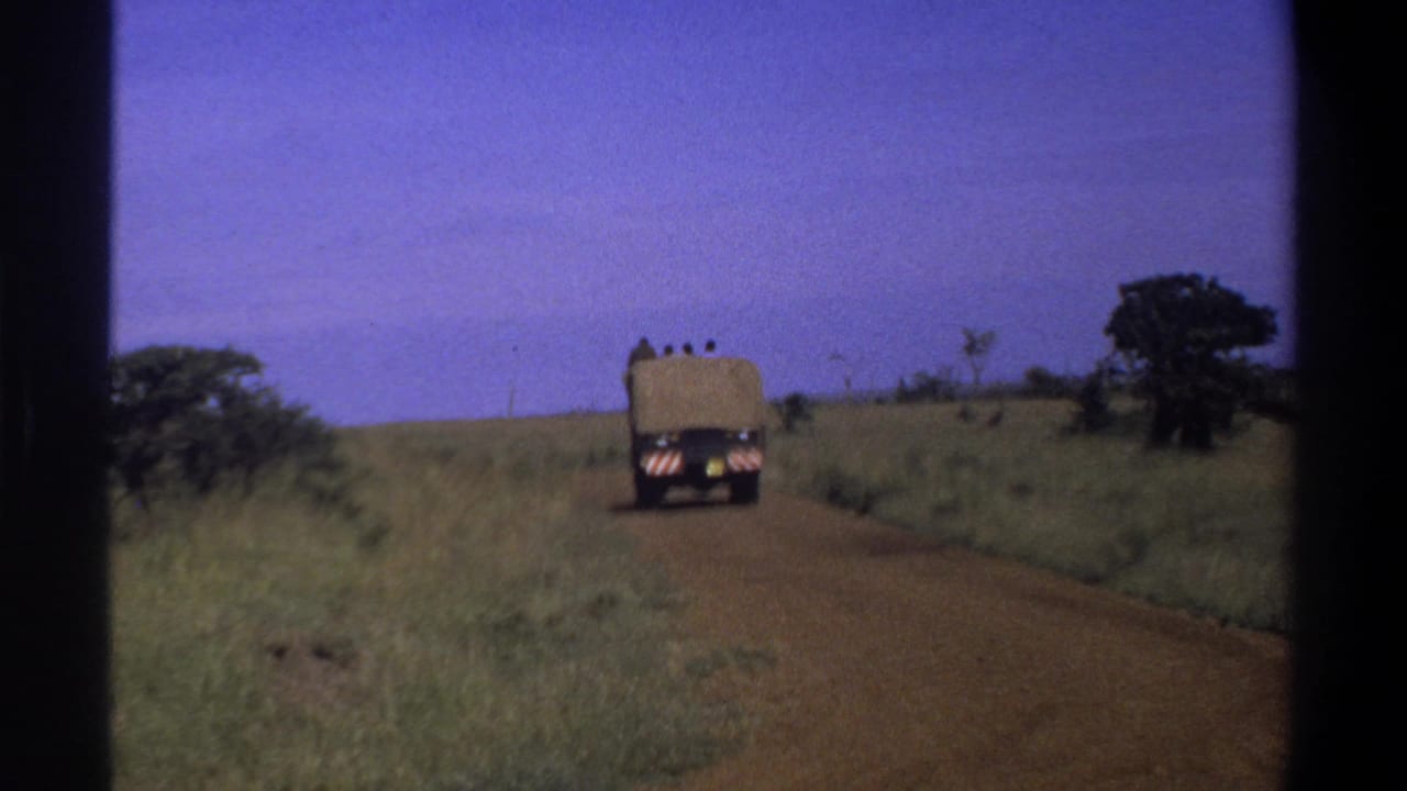 1969 Lagos, Nigeria 8mm frame showing a tarp-covered truck moving away along an unpaved road through open grassland.