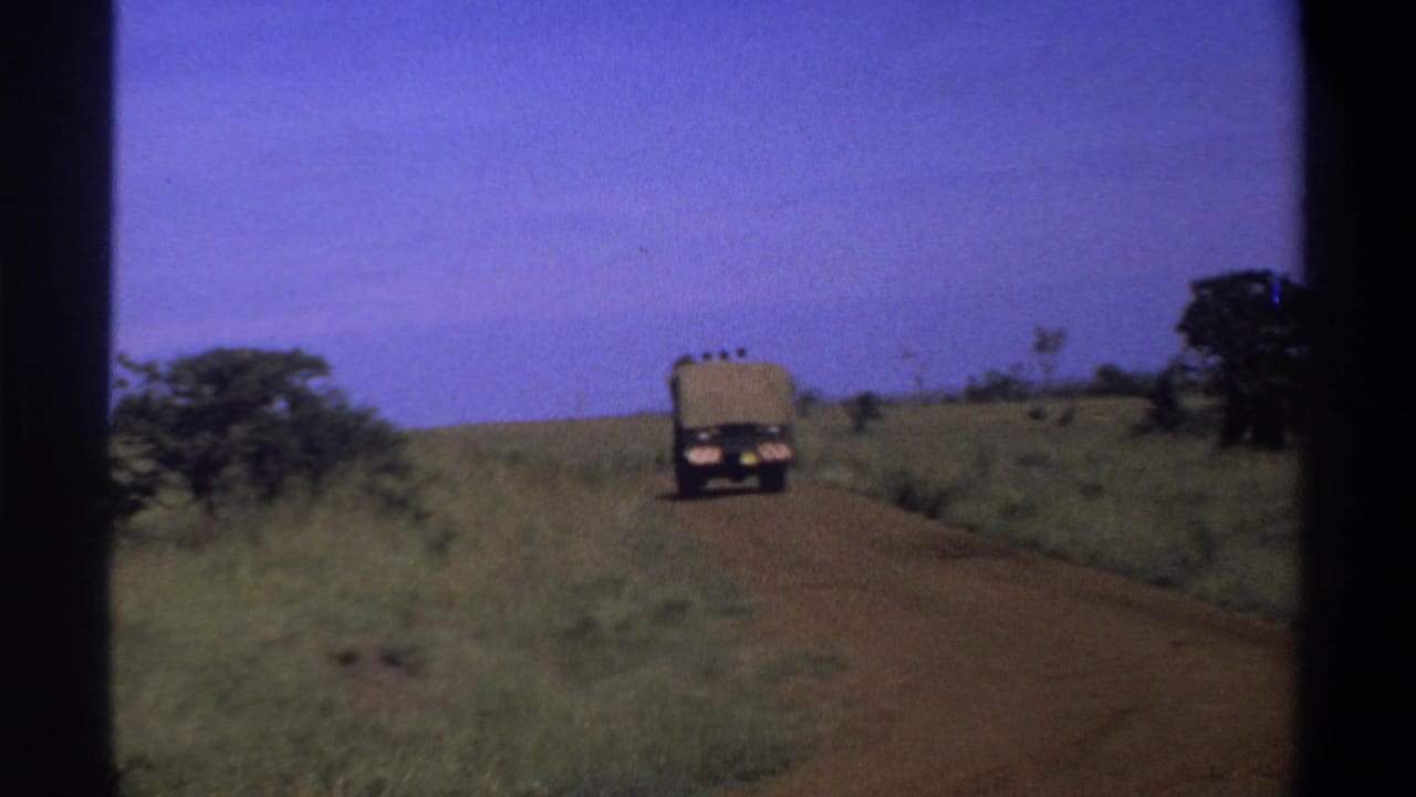 Distant truck continuing along a dirt road across open grassland.