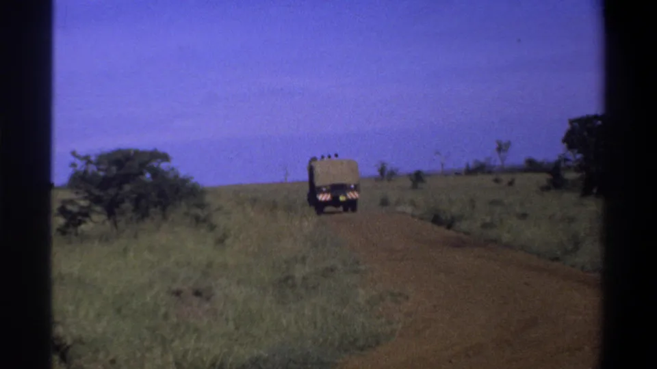 A distant canvas-covered truck continues along the dirt road in the 1969 Nigeria home-movie footage.