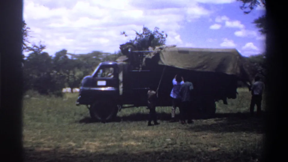 Several men stand near a canvas-covered truck in rural Lagos, Nigeria footage as cargo appears to be unloaded.
