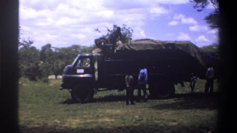 A 1969 Lagos home-movie frame shows men around a tarp-covered truck, with branches or cargo visible above the bed.