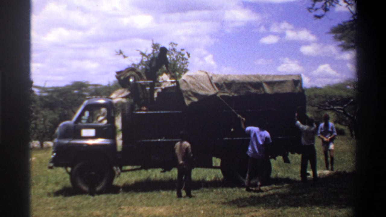 The 8mm frame shows several men around a covered truck in Lagos, with the vehicle filling most of the scene.