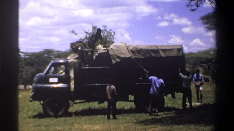 The 8mm frame shows several men around a covered truck in Lagos, with the vehicle filling most of the scene.