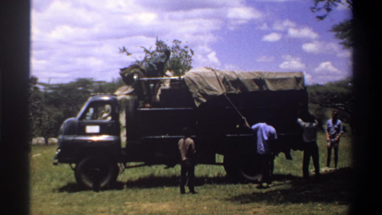 A group of men stands near the covered truck in 1969 Lagos footage, with rope or straps running from the tarp area.