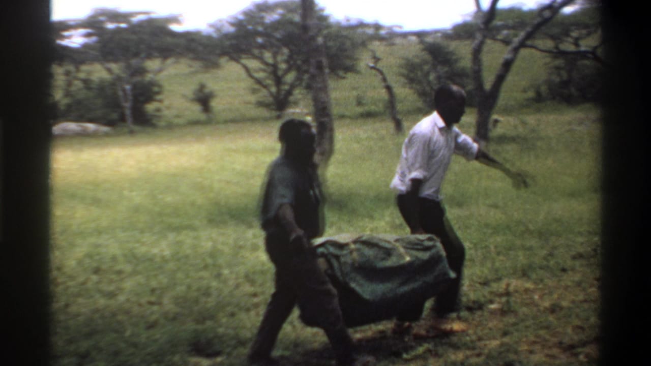 Two men continue carrying a covered sack rightward through grass near trees.