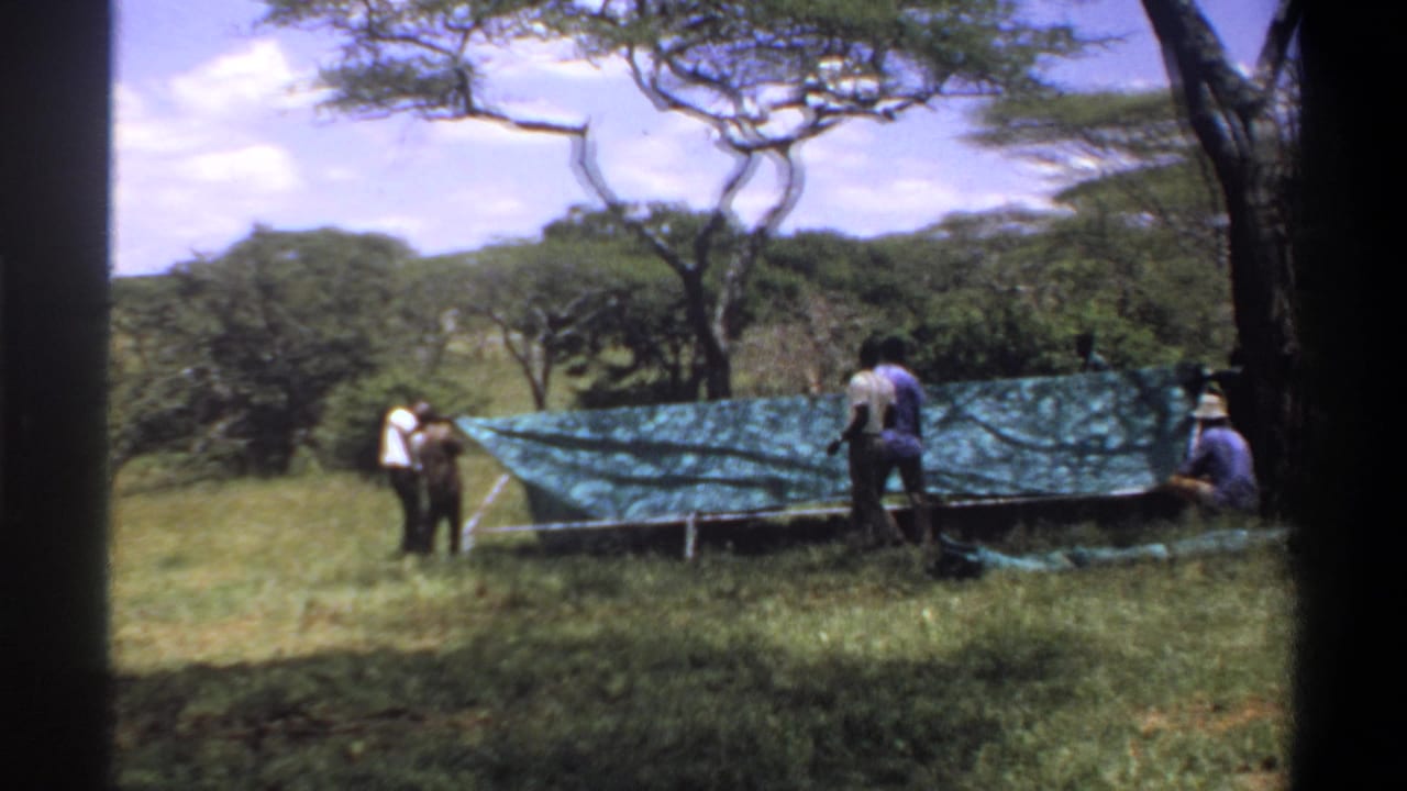 The final frame shows men beside a low tarp-covered structure in open grassland, with trees, hills, and 8mm frame edges visible.