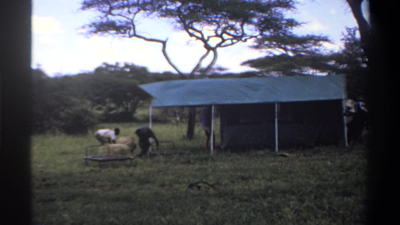 1969 Lagos-area home-movie frame showing people in a grassy clearing beside a canvas shelter, with trees behind them.