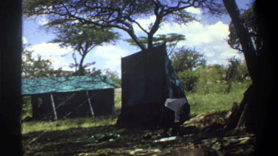 A dark tent or awning panel is raised in the Lagos outdoor setting, with one man partly visible near its base.