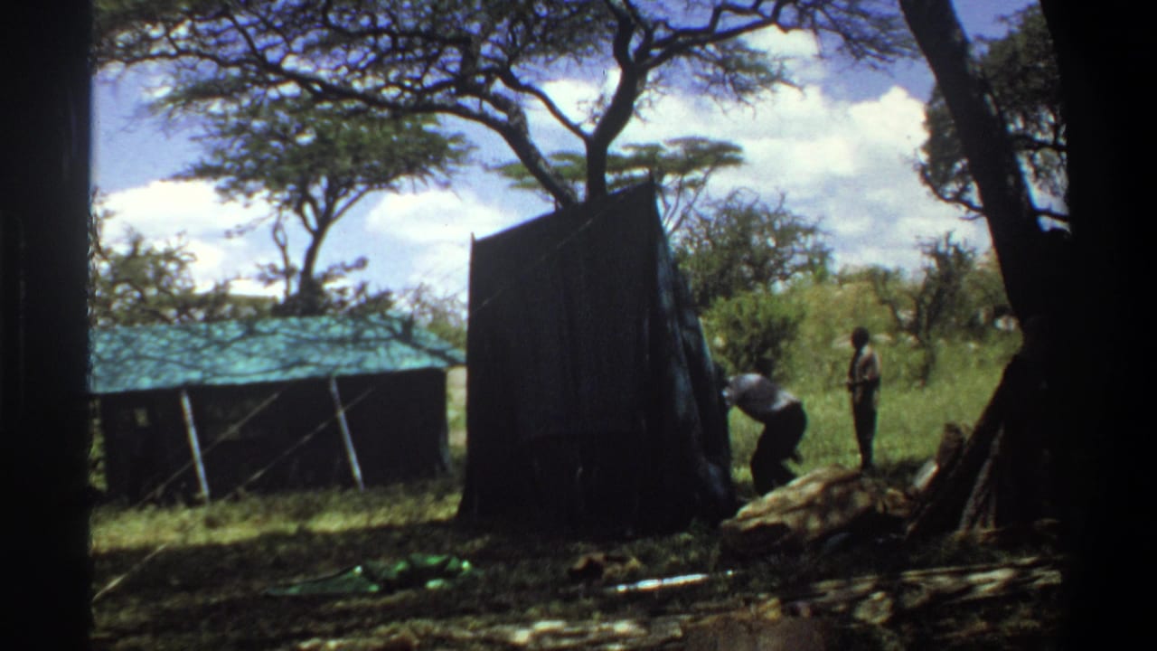 A man bends near a tent while another person stands in the grass.