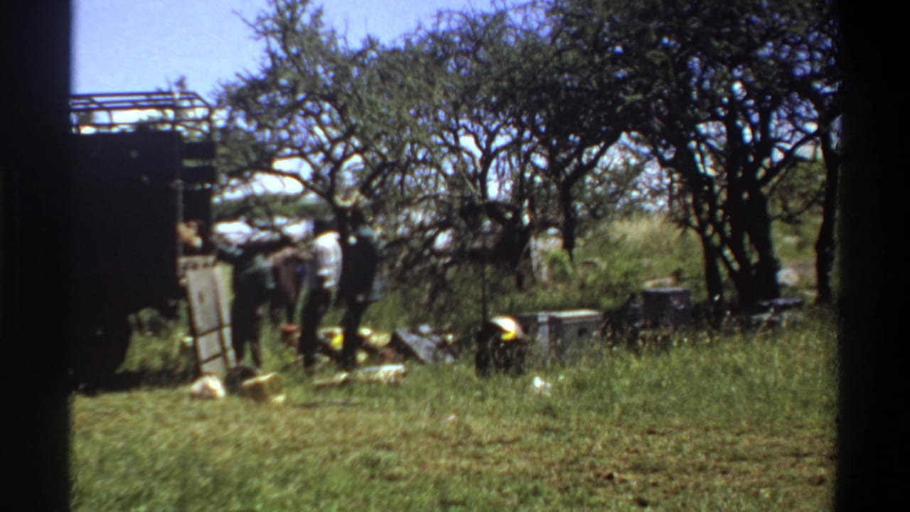 In 1969 Lagos home-movie footage, several workers appear beside a dark truck in a grassy, tree-lined farm setting.