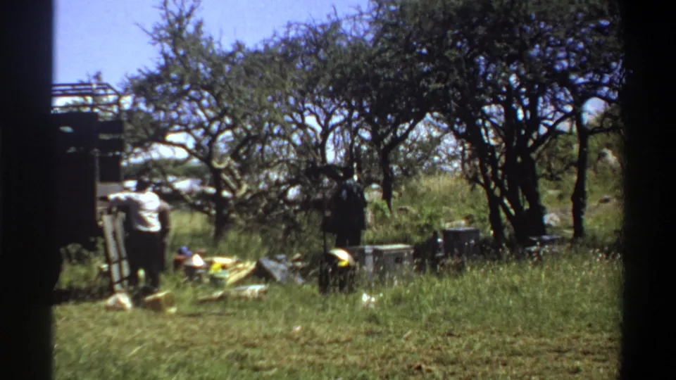 The 1969 Lagos home-movie frame shows men around a truck, with one bending near scattered supplies on the ground.