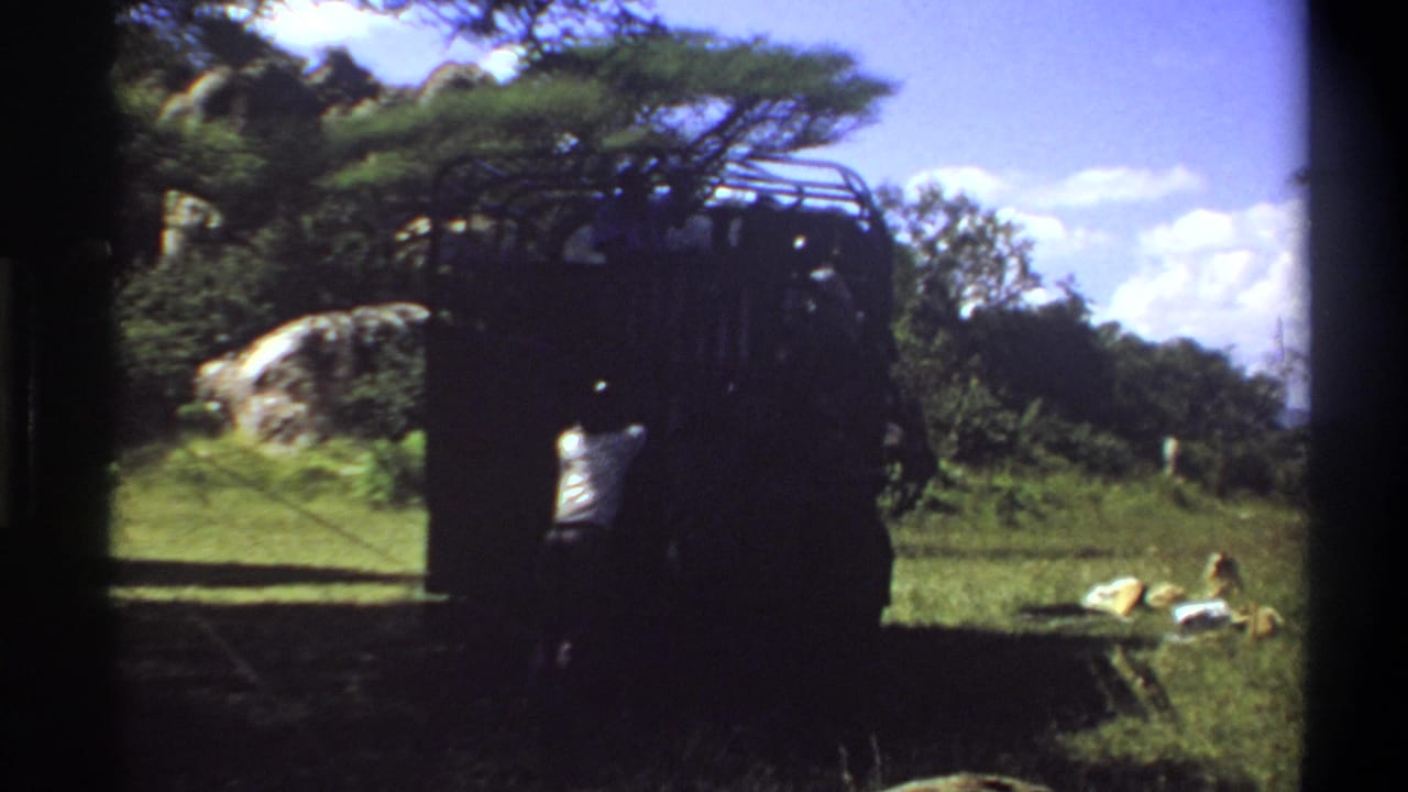 Final 1969 Lagos, Nigeria frame shows the dark roof-rack truck from a similar angle, with a person partly visible near the rear and greenery behind.
