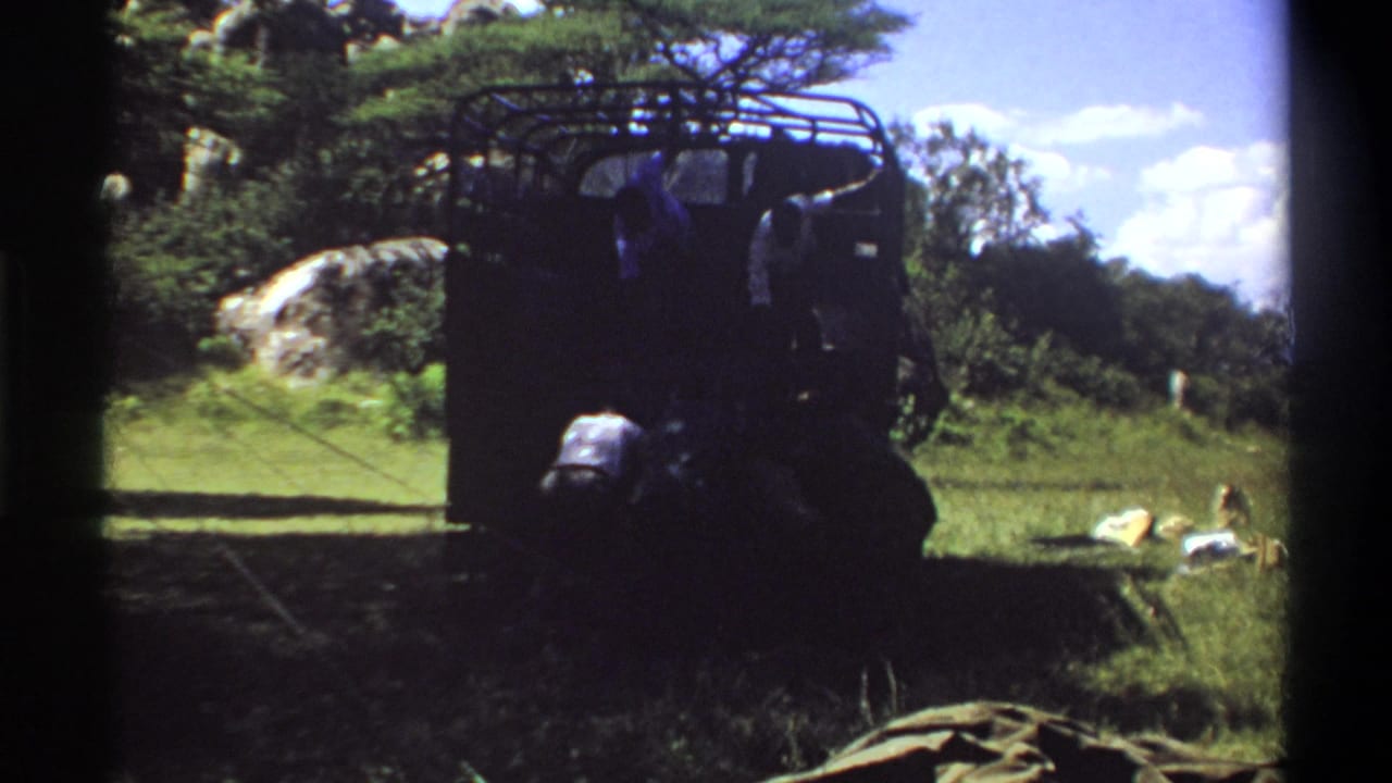1969 Lagos 8mm frame showing a person crouched near the rear of a dark truck, with other people partly visible by the vehicle.