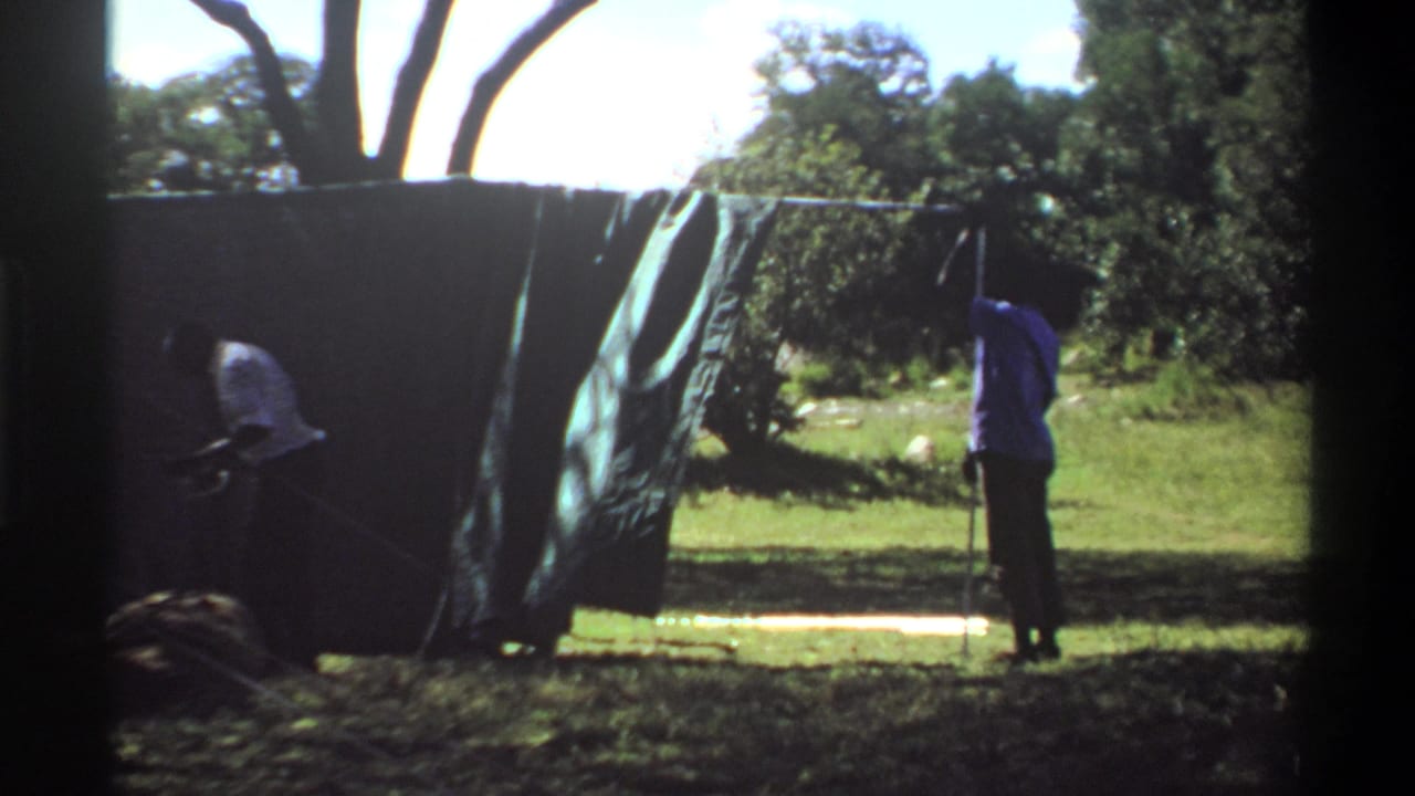 Men continue setting up a large canvas tent in a bright outdoor camp scene, with the 1969 Lagos location supported by clip metadata.