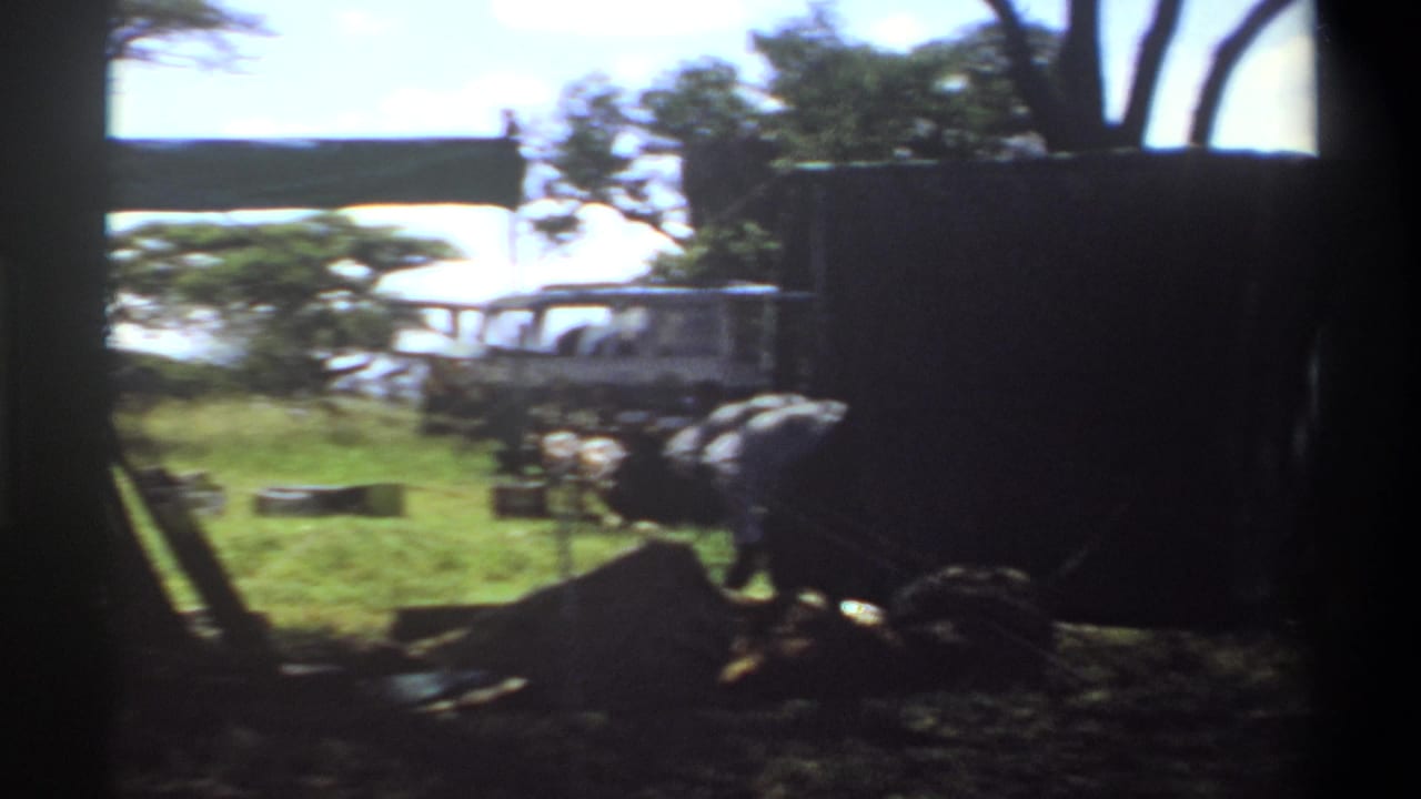 The closing frame places the dark tarp in the foreground, with a white vehicle, trees, grass, and scattered camp materials visible in Lagos, Nigeria, 1969.