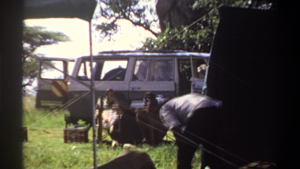 1969 Lagos campsite footage shows a closer view of the parked white utility vehicle, dark shelter, ropes or lines, and a man working near camp materials.