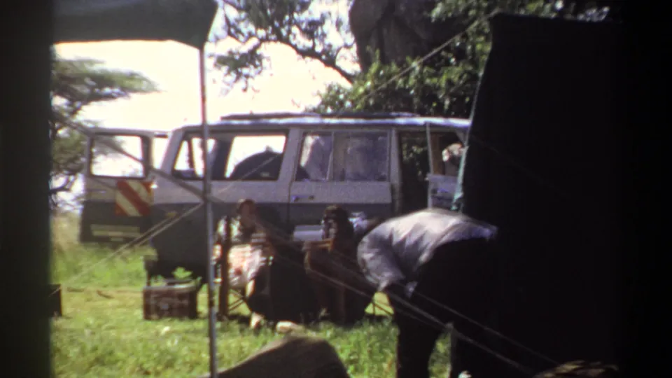 1969 Lagos campsite footage shows a closer view of the parked white utility vehicle, dark shelter, ropes or lines, and a man working near camp materials.